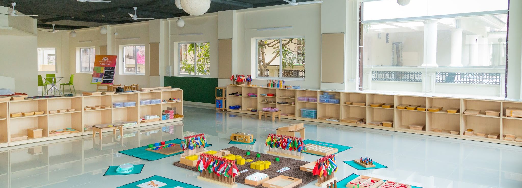 A Children&rsquo;s House before the day begins: open shelves at child height along two walls, and Montessori materials set out on mats across the floor &mdash; number rods, the flag stand, sensorial work and cards.